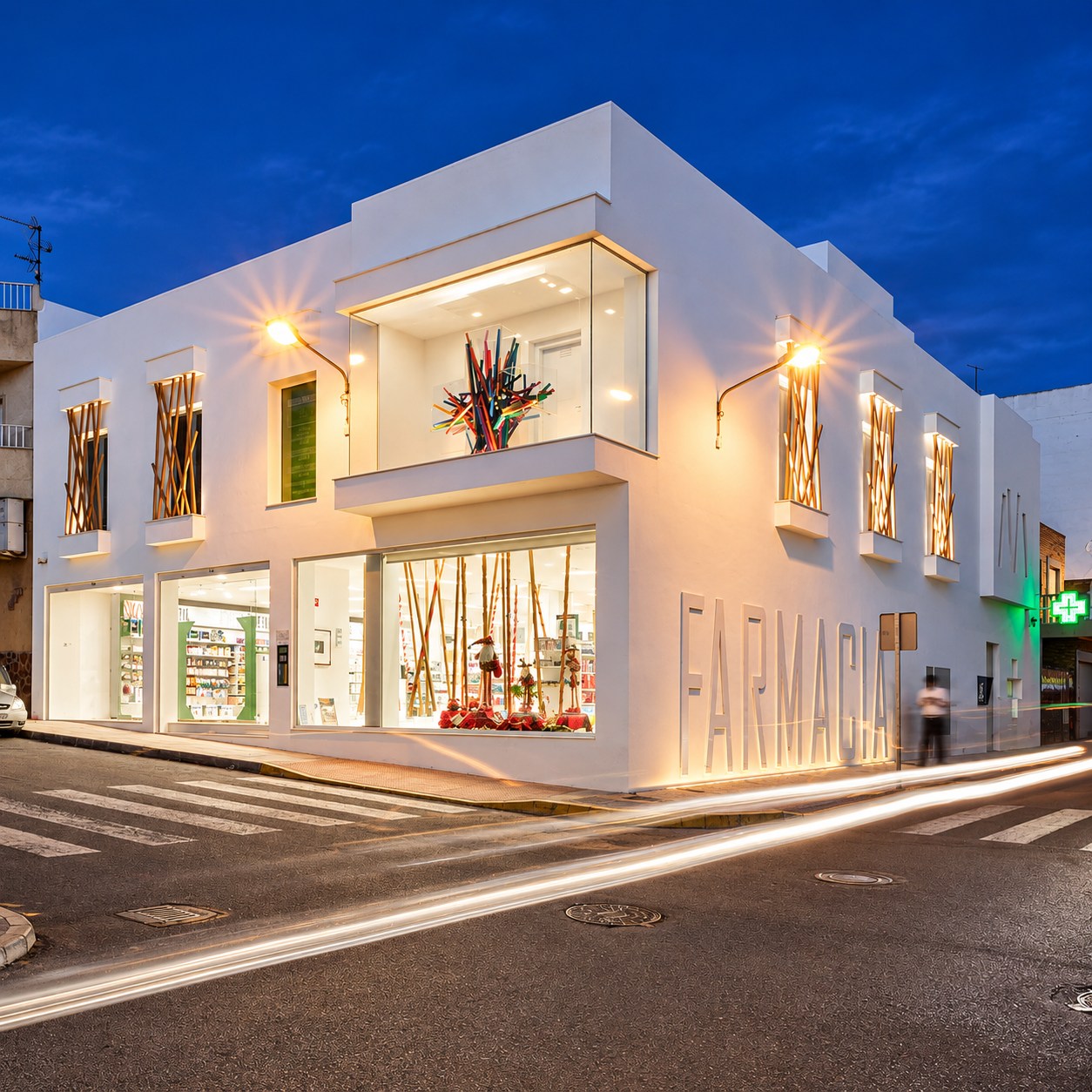 Fachada nocturna de Farmacia Caparrós y Reina con iluminación exterior y grandes huecos acristalados